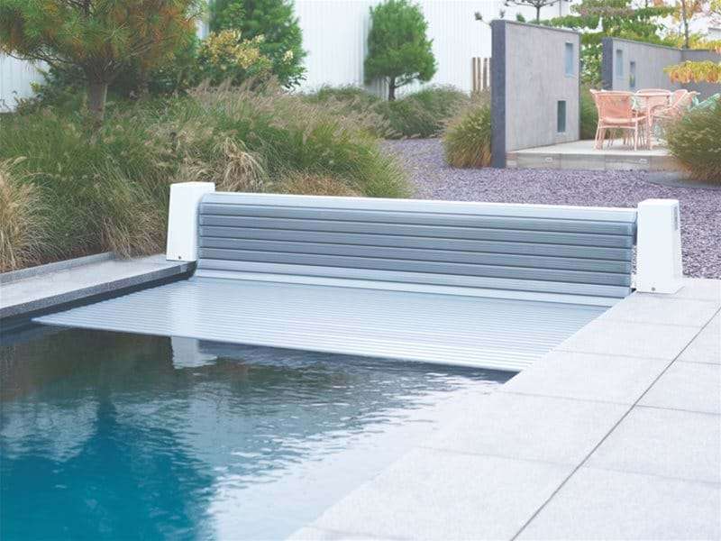automatic slatted pool cover half open over a one piece swimming pool.