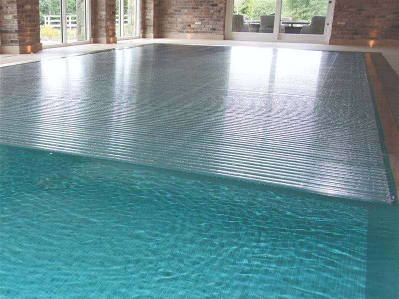 automatic slatted pool cover half open over a one piece swimming pool.
