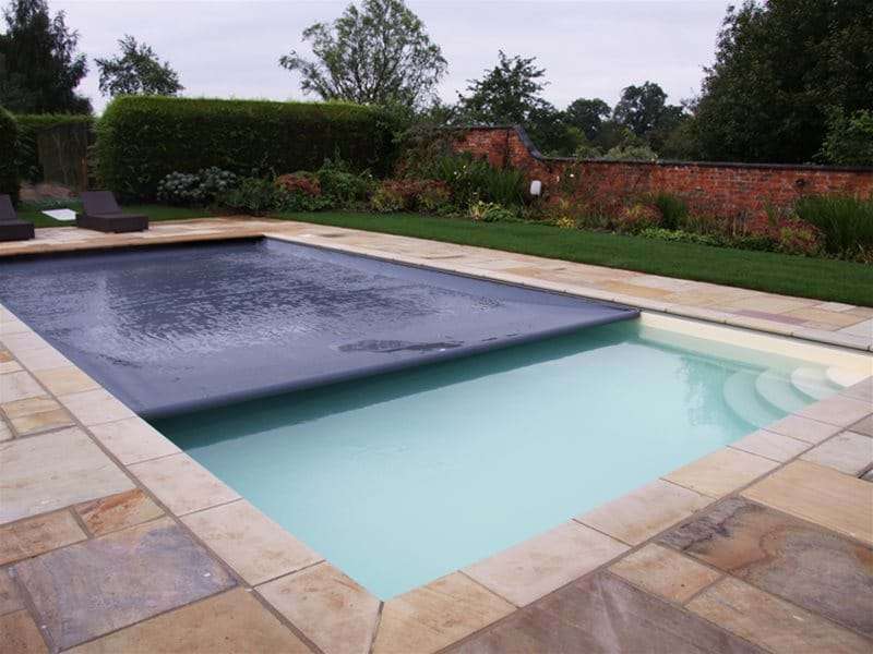 automatic safety pool cover half closed over a one piece swimming pool.